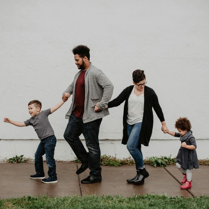 A joyful family walking together outdoors, holding hands in a playful and happy moment.